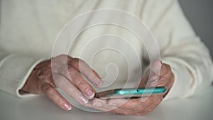 Old woman with wrinkled hands slides pages on mobile phone