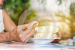 Old women hand hold fake teeth ready eat with corn on dish background