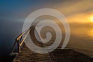 Old wood jetty reaching into foggy lake in morning twilight