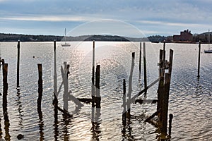 Old wood pilings ruins with a sailboat in the distance