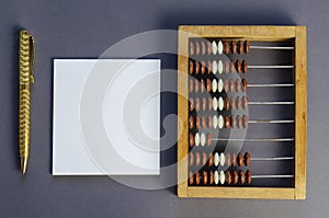 Old wooden abacus, square blank white paper gold-colored pen on gray background
