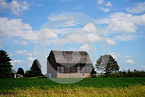 Old wooden abandoned farm barn sits on a farm field outside of fond du Lac, Wisconsin during a blue cloudy day.