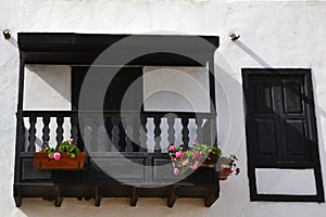 Old wooden balcony decorated with flowers on a traditional canarian white house.