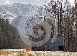 An old wooden barn sits beneath a snow covered mountain in the Smokies.