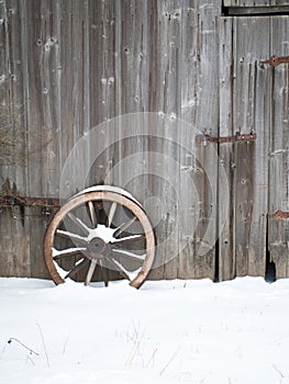 Old wooden barn wall with an old wooden cartwheel in snow