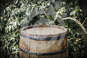 Old wooden barrel as a table with space for an advertising product. Green plants garden background.