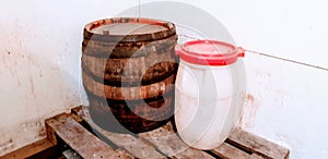 Old wooden barrel with metal rings and big white plastic container with red cap