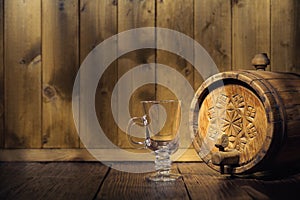 Old wooden barrel with a tap and an empty glass cup in the twilight on a wooden background