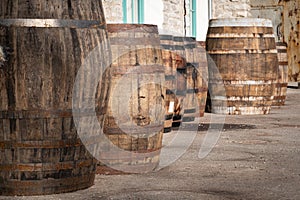 Old wooden barrels or casks at brewery backyard on a sunny day. Wine or beer oak vintage containers with stone wall texture