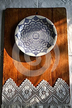 old wooden board on a white linen tablecloth and a white plate with a blue pattern lace towel sunny natural light,