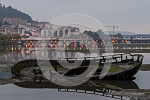 Old Wooden Boat Decaying in the Sand at Eume River Pontedeume in the Background with lighted bridge La CoruÃ±a Galicia