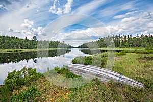 Old wooden boat on the lake shore, surrounded by endless pine forest reflected in the lake