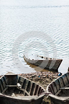 Old, wooden boat sunken near by the muddy, littered shore