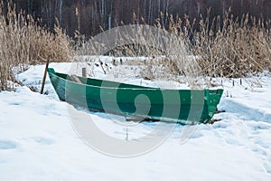 Old wooden boats lie in the snow on the shore of an ice-covered frozen lake in the winter.
