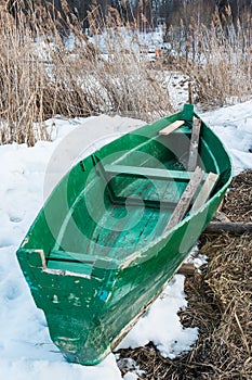 Old wooden boats lie in the snow on the shore of an ice-covered frozen lake in the winter.