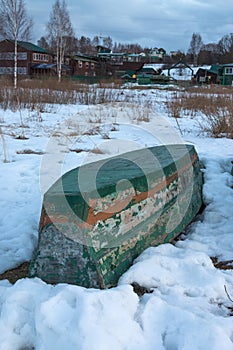 Old wooden boats lie in the snow on the shore of an ice-covered frozen lake in the winter.