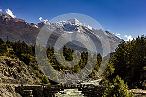 Old wooden bridge over marsyandgi river and snowy mount pisang peak in the background in annapurnas of nepal