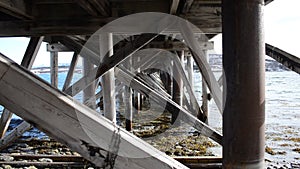 Old wooden bridge underbelly covered in old barnacles with calm waves and bright sunshine