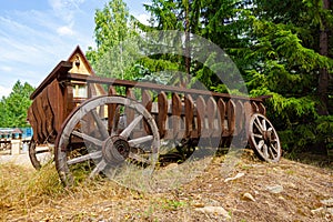An old wooden broken cart with wheels stands in nature in the village on a summer sunny day. The iron is rusty. Close-up