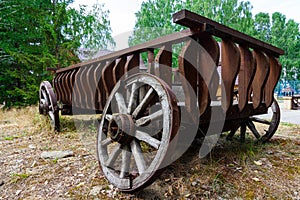 An old wooden broken cart with wheels stands in nature in the village on a summer sunny day. The iron is rusty. Close-up