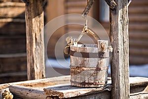 Old wooden bucket of water hanging over the well with a wooden building