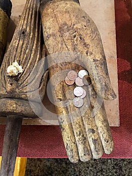 Old wooden Buddha hand with little one thai baht money coins inside, offerings and donation buddhist symbol