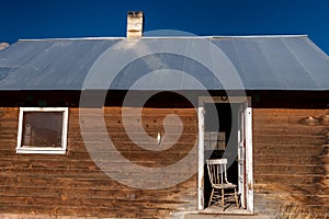 Old wooden cabin in morning light with chair in doorway