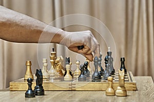 Old wooden chess pieces on chessboard. Hand of adult man making move with white pawn
