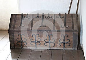 An old wooden chest, bound with decorative metal plates, is installed in the corner of the room