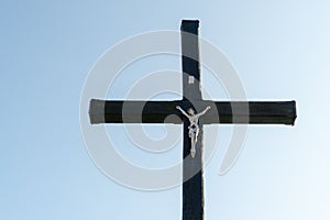 An old wooden Christian cross against a clear blue sky on a beautiful summer day. A statuette of Jesus in the center of the cross