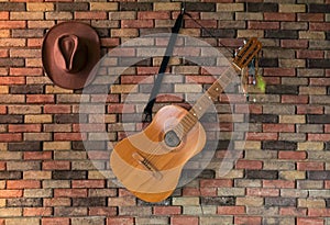 Old wooden classic guitar and cowboy hat hanging on brick wall