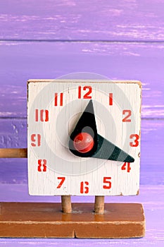 Old wooden clock toy for learning kids time. Second hand educational toy on purple wooden background. Marks and scratches