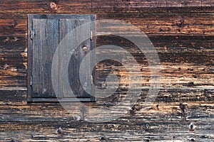 Old wooden closed window with metal hinges on an old wooden wall