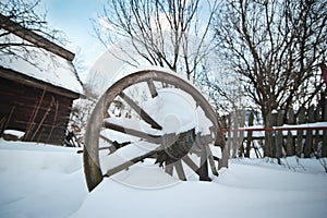 Old wooden cottage and wooden Romanian wheel covered by snow. Cold winter day at countryside. Traditional Carpathian mountains