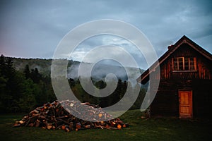 Old wooden country house in village. Fog, firewood, sunset, darkness
