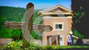 Old wooden cross in cemetery with small church on sunny day with little girl running in background