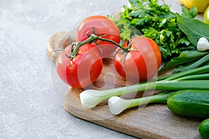 Old wooden cutting board with fresh vegetables on stone concrete table. Close-up view on salad ingredients: tomatoes, cucumbers,