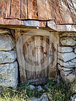 Old wooden decayed door on the stone mountain cottage house with old lock and traditional stone walls. Rusty roof on top and