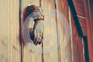 Old wooden door with a brass metal sounder in the form of a small hand to knock on the door.