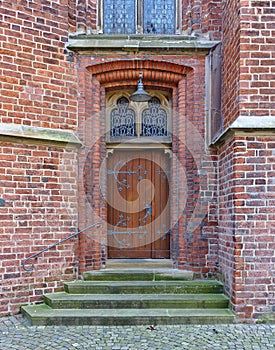 Old wooden door in brick wall with iron fittings, steps and ornamental windows