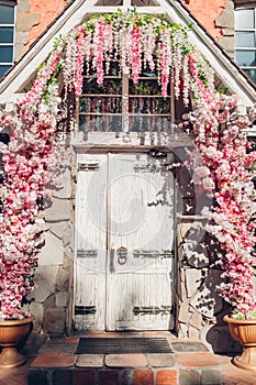 Old wooden door decorated with white and pink flowers. Exterior design. Cafe entrance