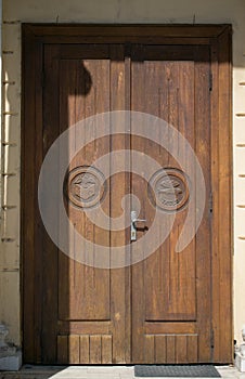 Old wooden door at the entrance to a catholic church. There are different religious symbols on the door