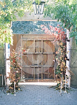 Old wooden door with flowers, chandelier and candles on a stone floor under arch plants