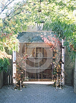 Old wooden door with flowers, a chandelier and candles on a stone floor under arch plants