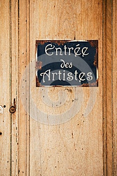 Old wooden door and metal plate with text `entry of the artists`