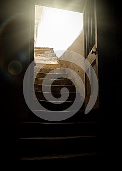 Old wooden door open into basement with light rays shining into dark creepy cellar from stone worn staircase, rundown with shadows