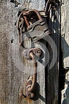 Old wooden door with padlock and rusty iron handle.