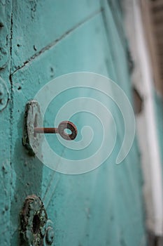 Old wooden door painted with cracked green paint and rusty key in the keyhole