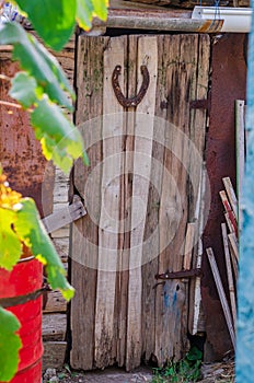 Old wooden door of a rustic barn. A large rusty metal horseshoe nailed to the door.