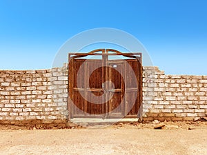 Old wooden door in white brick wall under blue sky in desert landscape. Constructions and architecture of the Egyptian desert